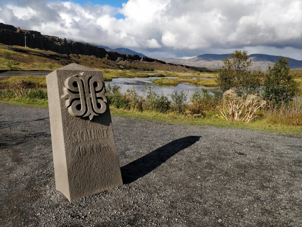 A stone waymarker reading "Skalholt 49 KM" in Thingvellir National Park, Iceland.