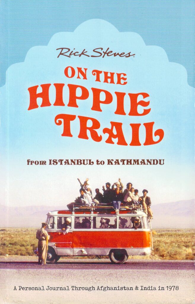 Cover for the book "On the Hippie Trail from Istanbul to Kathmandu" by Rick Steves, featuring an old photo of an orange and white short bus in a desert area, loaded with passengers inside and on the roof, being stopped by an official in a beige uniform.